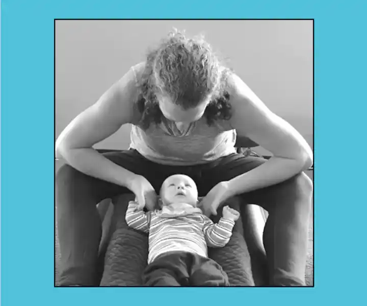 A woman is performing chiropractic care on a baby, gently holding the baby's arms while the baby is lying on a padded surface. The image is in black and white with a light blue background.